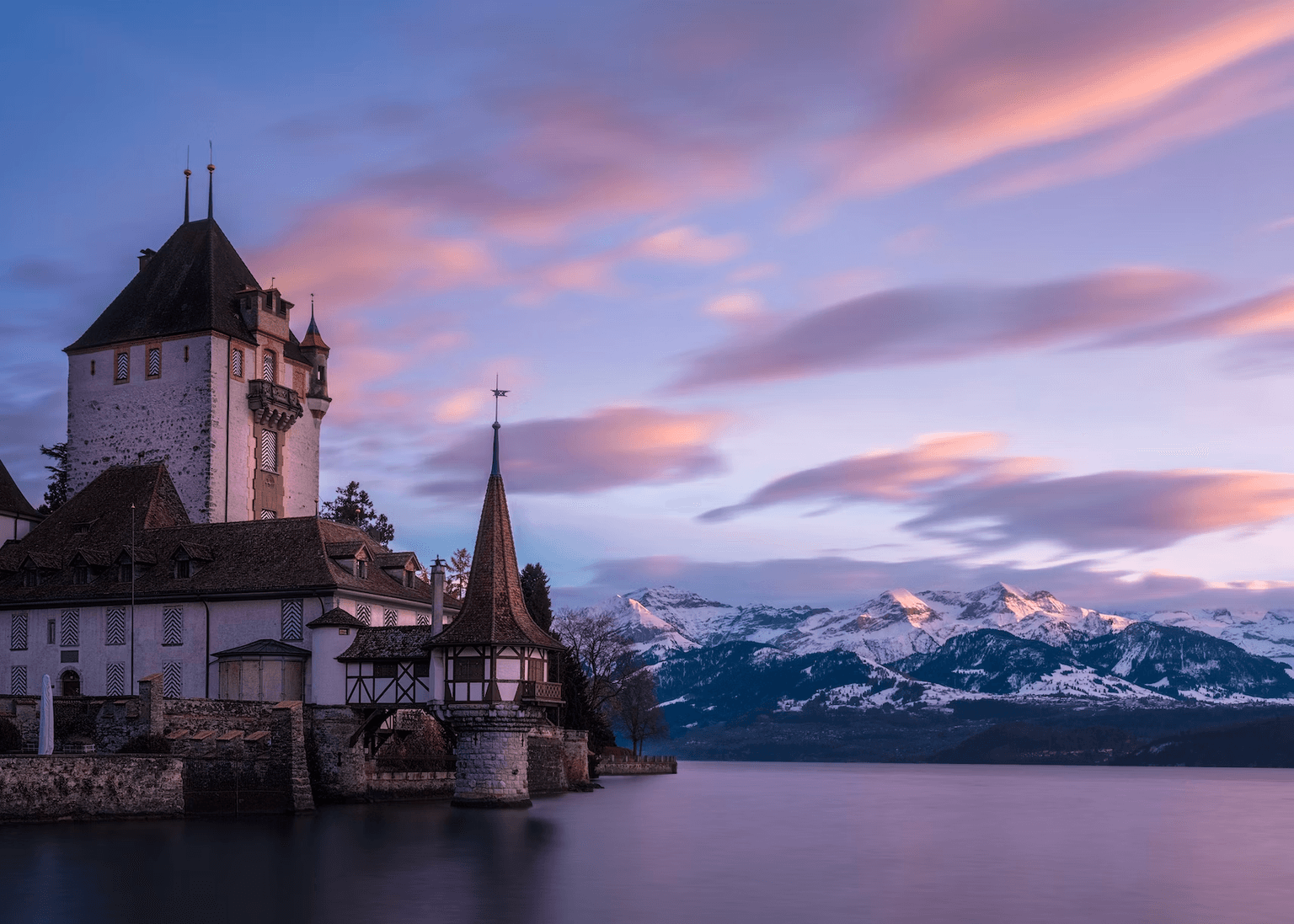 Castle at lake at sunset with mountains in background